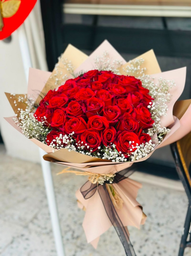 Açık pembe ambalajda beyaz çiçeklerle çevrelenmiş kırmızı gül buketi